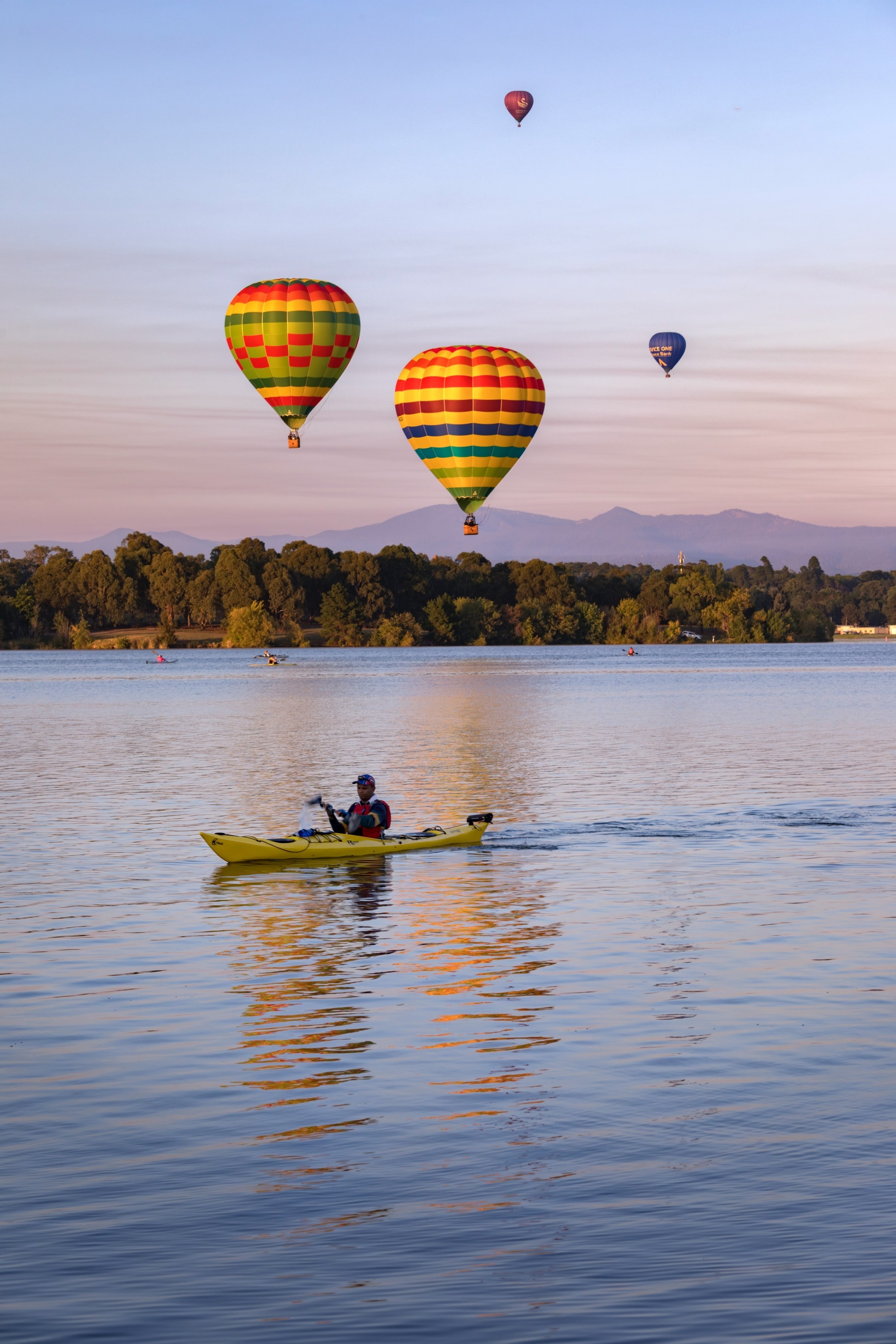 Een kajakker peddelt een rivier af in Canberra, Australië, terwijl er luchtballonnen overvliegen
