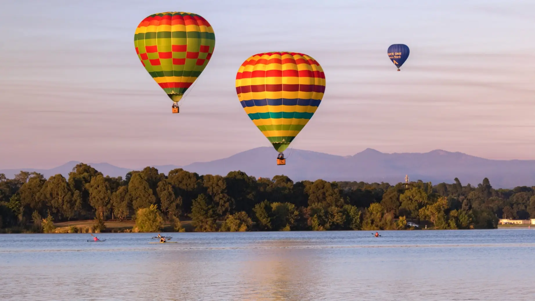 Ein Kajakfahrer paddelt auf einem Fluss in Canberra, Australien, während über ihm Heißluftballons fliegen