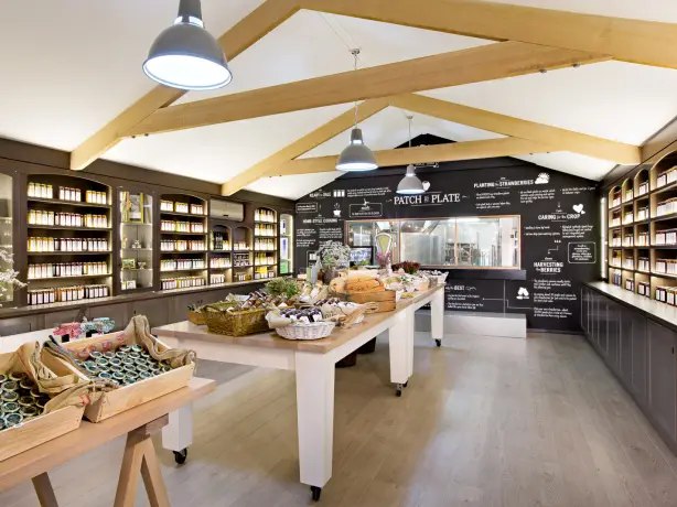 Hofladen mit Regalen mit Eingemachtem, Holztischen mit lokalen Produkten und einer Kreidetafel hinter dem Tresen.