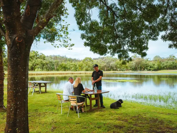 Ehepaar bei einer geführten Weinprobe an einem See mit einem schwarzen Hund in Australien