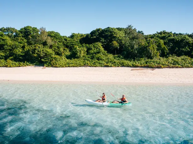 Australien, Queensland, Cairns - Ein Paar fährt mit dem Kajak entlang der Küste, mit Sandstrand und Wald im Hintergrund.