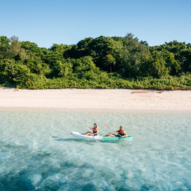 Australien, Queensland, Cairns - Ein Paar fährt mit dem Kajak entlang der Küste, mit Sandstrand und Wald im Hintergrund.