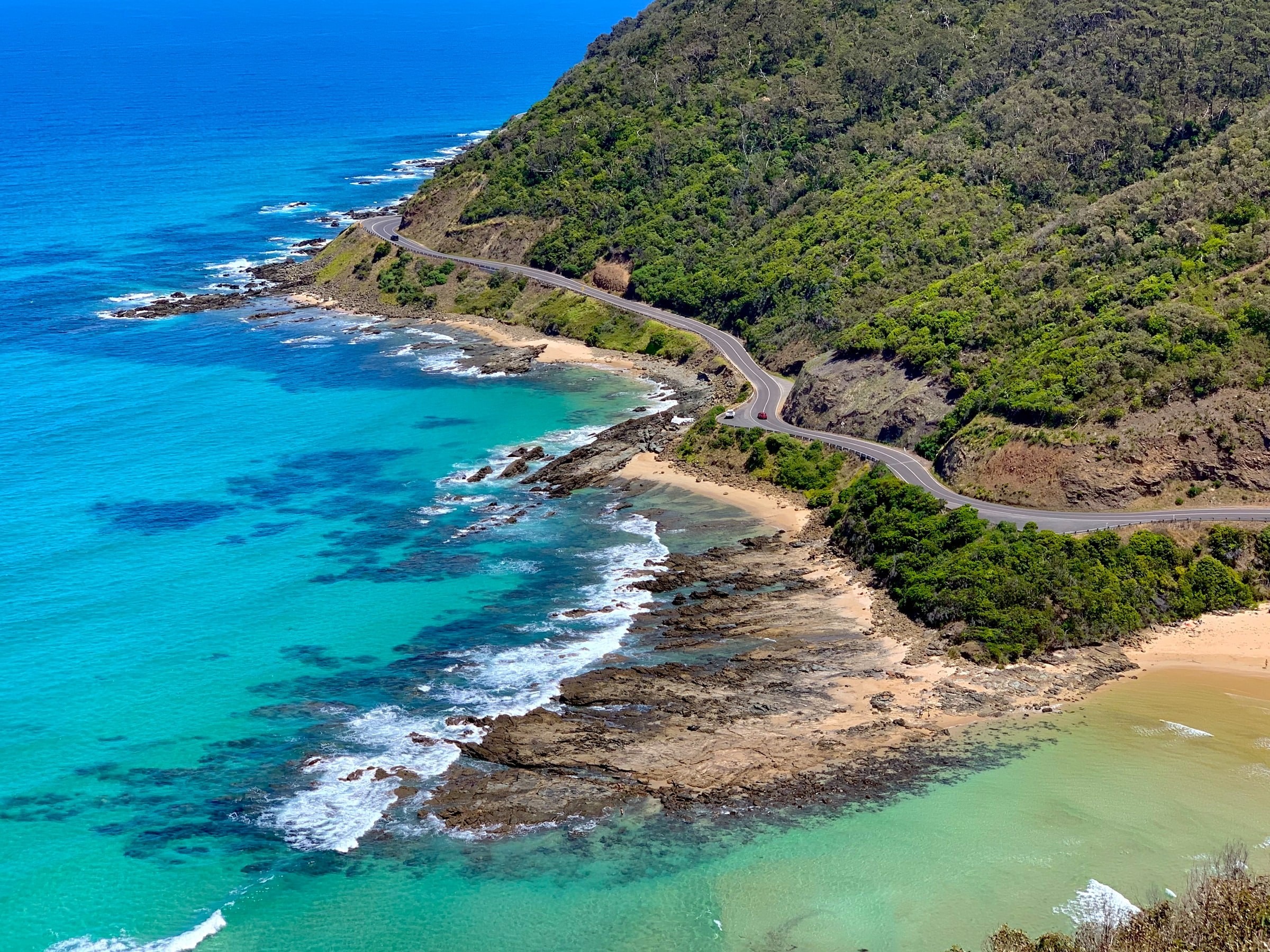 A wide angle shot of cars driving along the Great Ocean Road in Victoria, Australia
