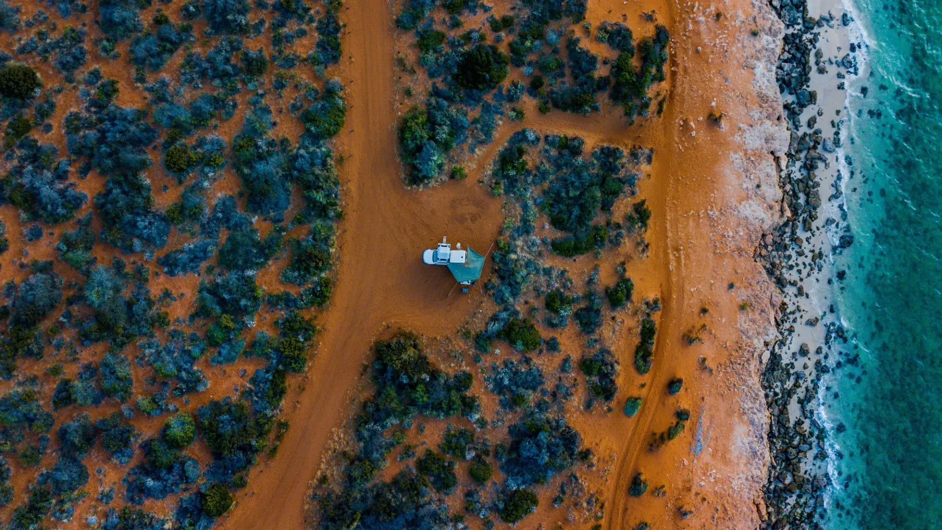 Vogelperspektive auf Camper, der auf rotem Sand an der Küste steht