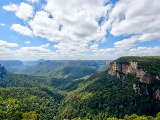 Eine Landschaftsansicht der Blue Mountains in New South Wales, Australien, mit üppig grünen Bäumen und blauem/bewölktem Himmel.