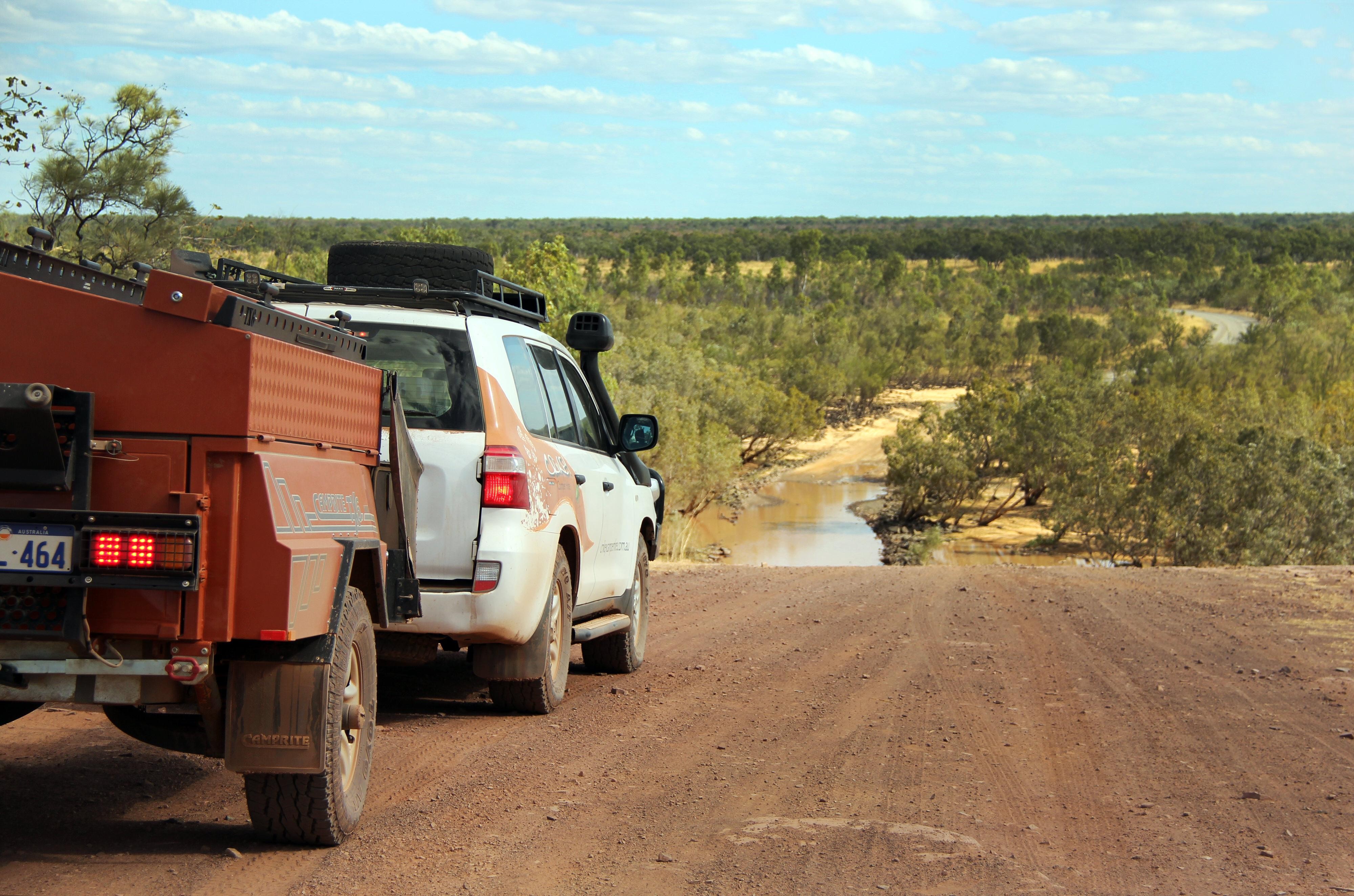 Witte auto met aanhanger op de Gibb River Road rijdt richting een overstroomde rivier om deze over te steken in de Australische outback