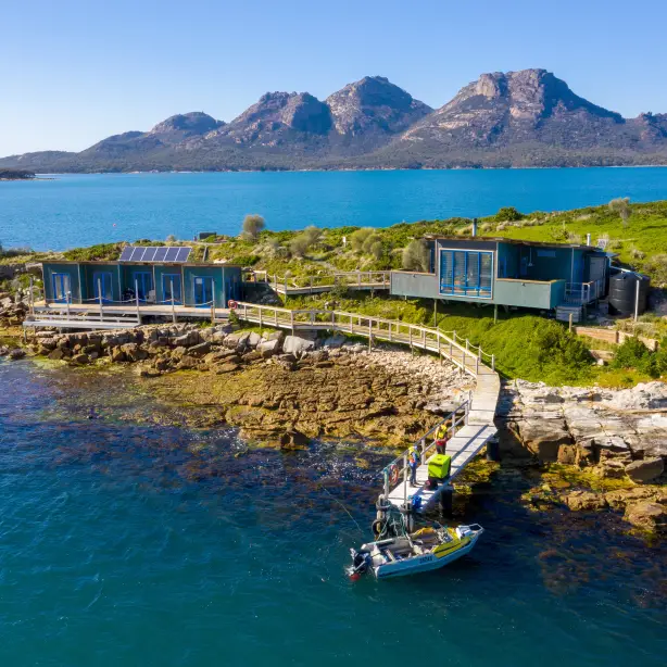 Insel mit Steg und zwei Gebäuden mit Bergen im Hintergrund