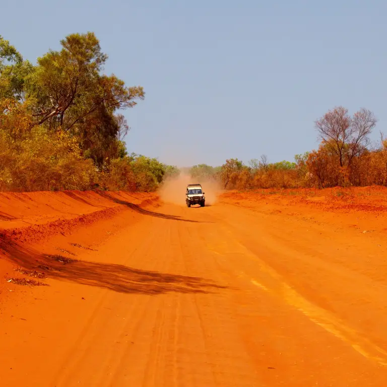 A car drives along a red dirt road in Alice Springs, Northern Territory, Australia