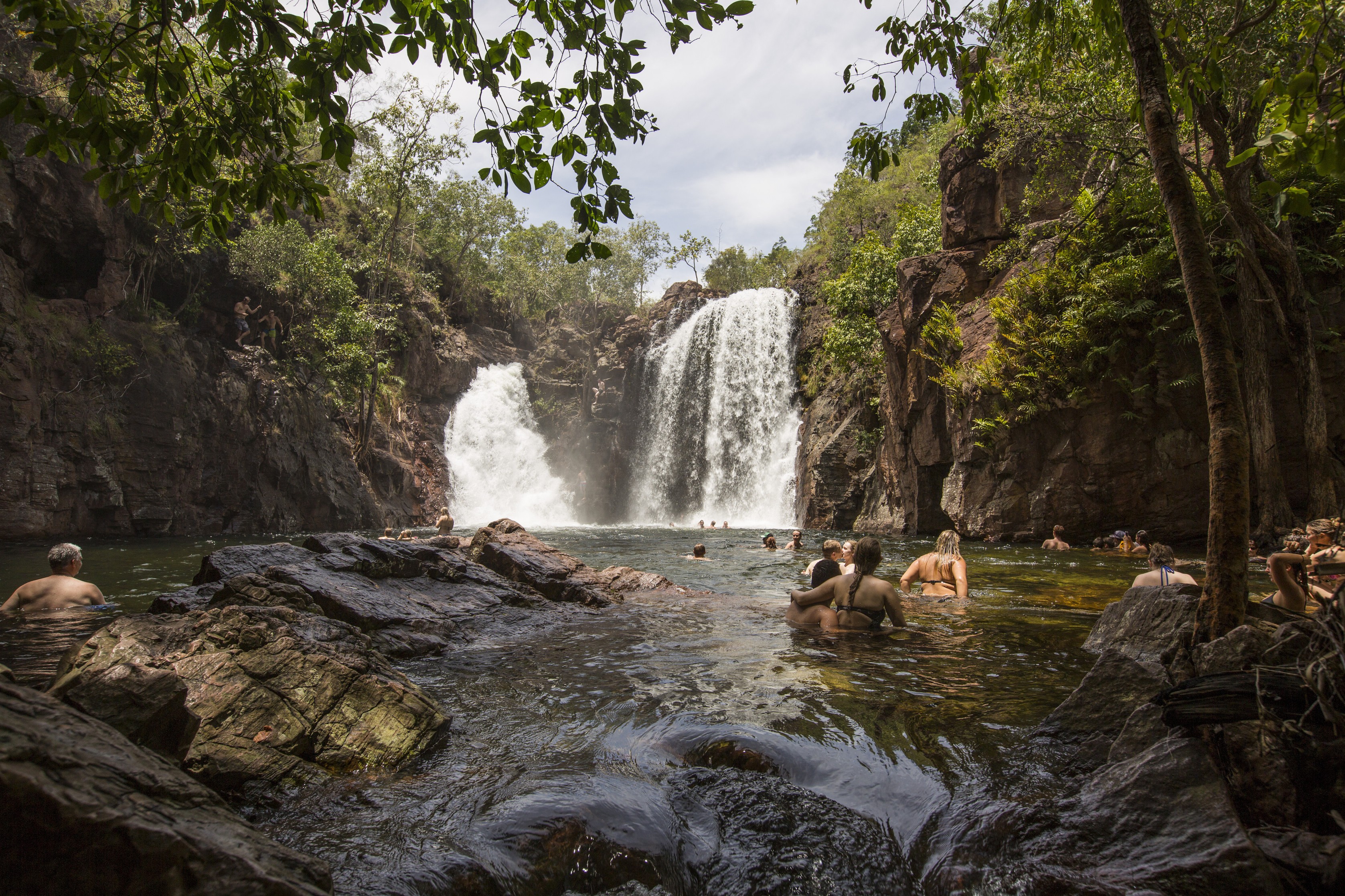 Menschen schwimmen in einem Felsbecken unter einem Wasserfall im Litchfield National Park, Australien
