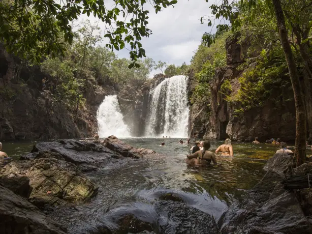 Menschen schwimmen in einem Felsbecken unter einem Wasserfall im Litchfield National Park, Australien