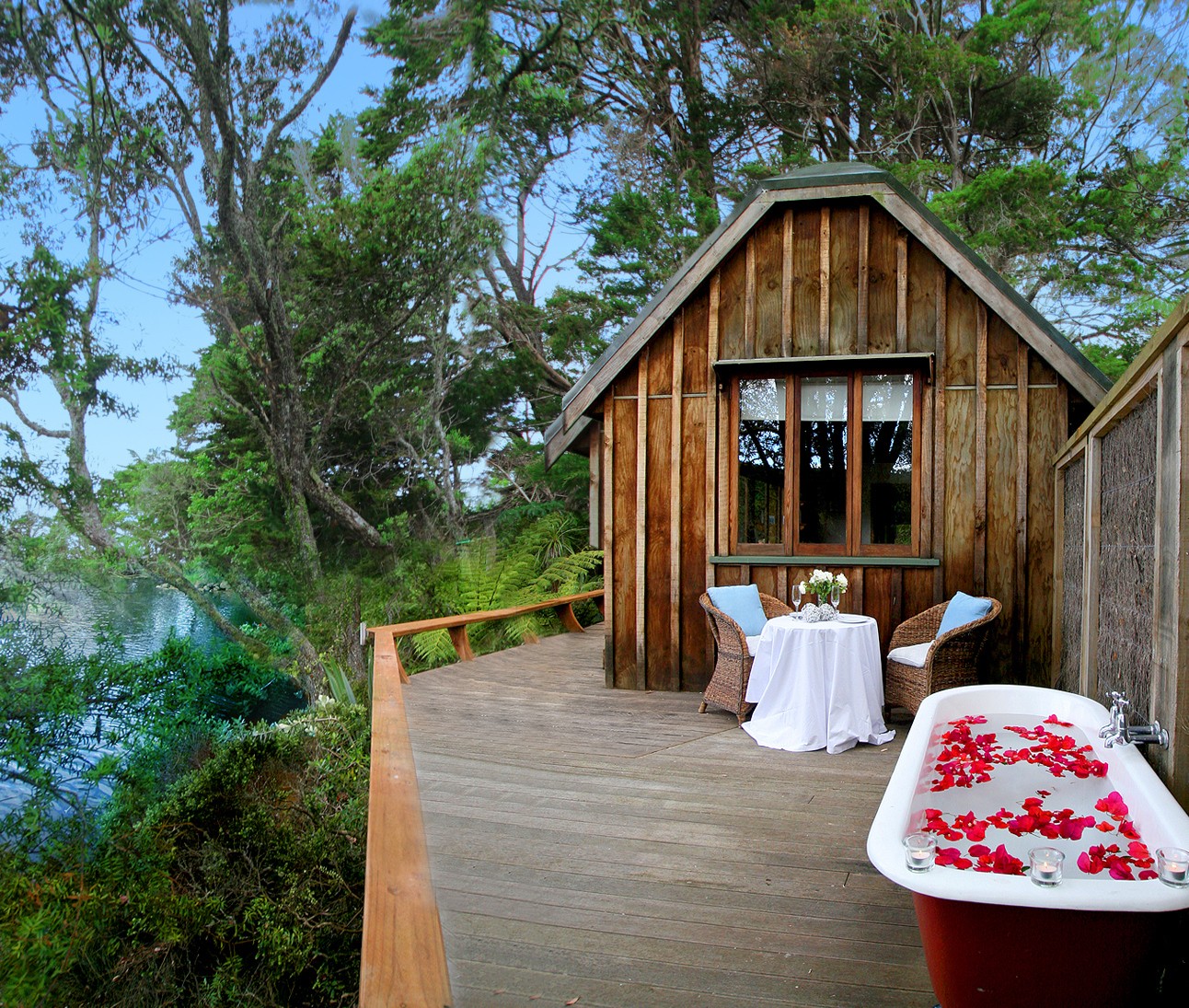 Terrasse mit Außenbadewanne mit Rosenblättern und einem Tisch und zwei Stühlen mit Blick auf Wald und Wasser