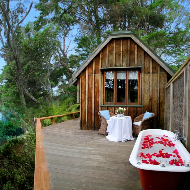 Terrasse mit Außenbadewanne mit Rosenblättern und einem Tisch und zwei Stühlen mit Blick auf Wald und Wasser