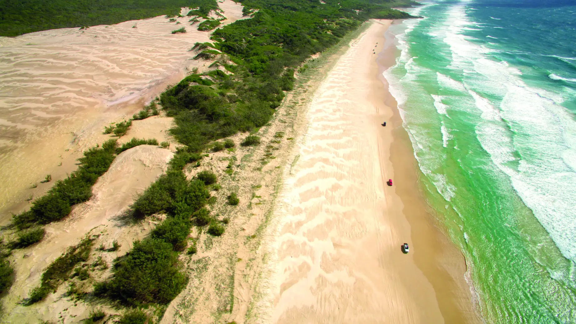 Der größte Sandstrand der Welt auf Fraser Island mit Dünen links und dem türkisgrünen Meer rechts