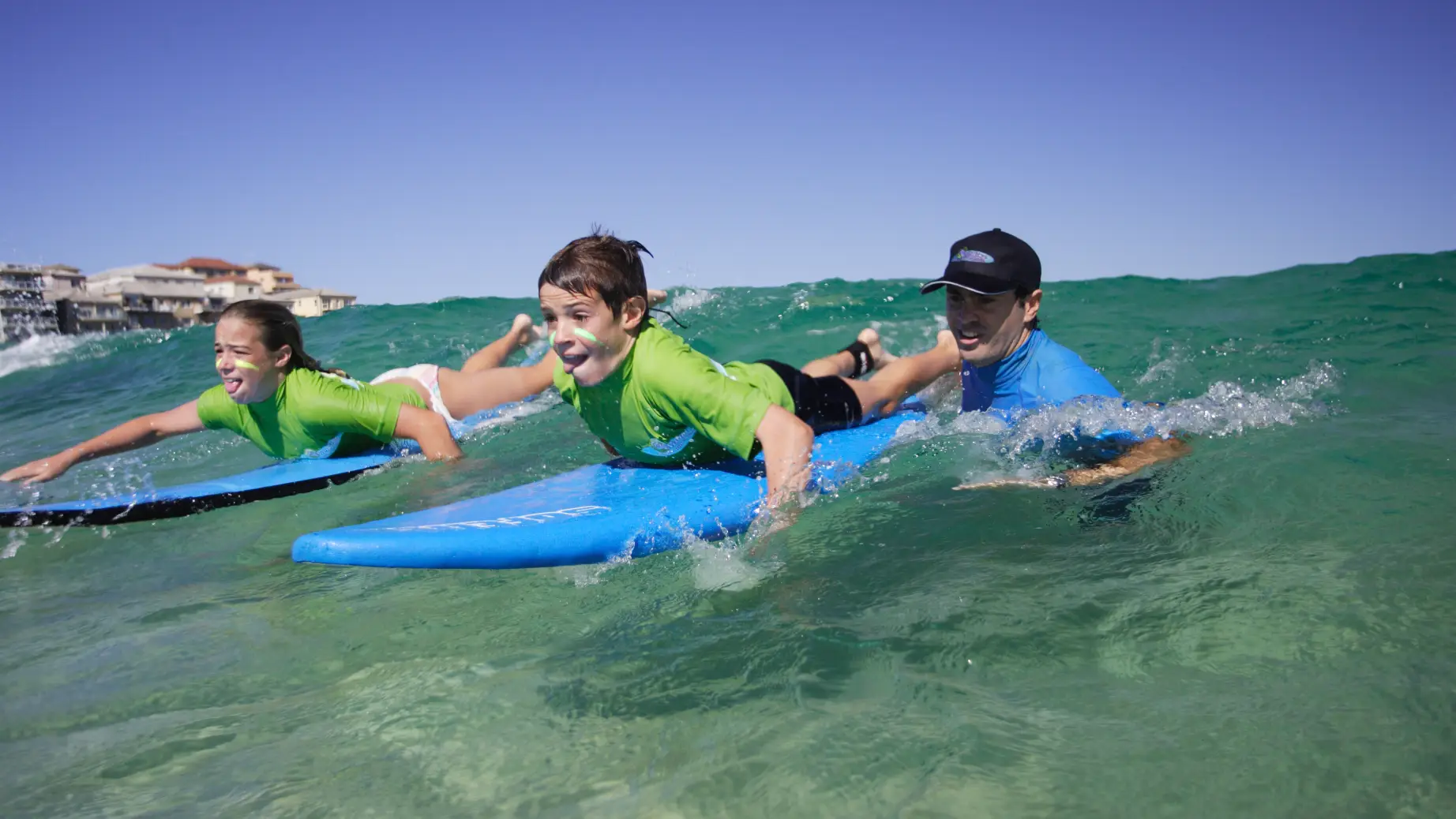 Zwei Kinder lernen mit einem Surflehrer das Surfen