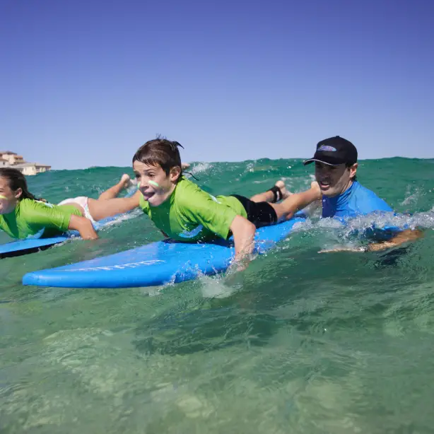 Zwei Kinder lernen mit einem Surflehrer das Surfen