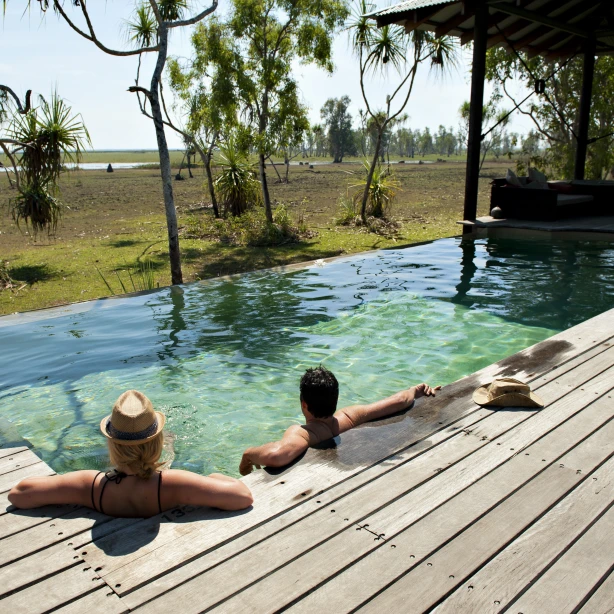 Two people sitting in a swimming pool looking out at the wild bush beyond in Australia