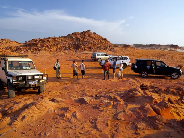 Eine Gruppe von Menschen steht neben vier Geländewagen in einer felsigen orangefarbenen Wüstenlandschaft