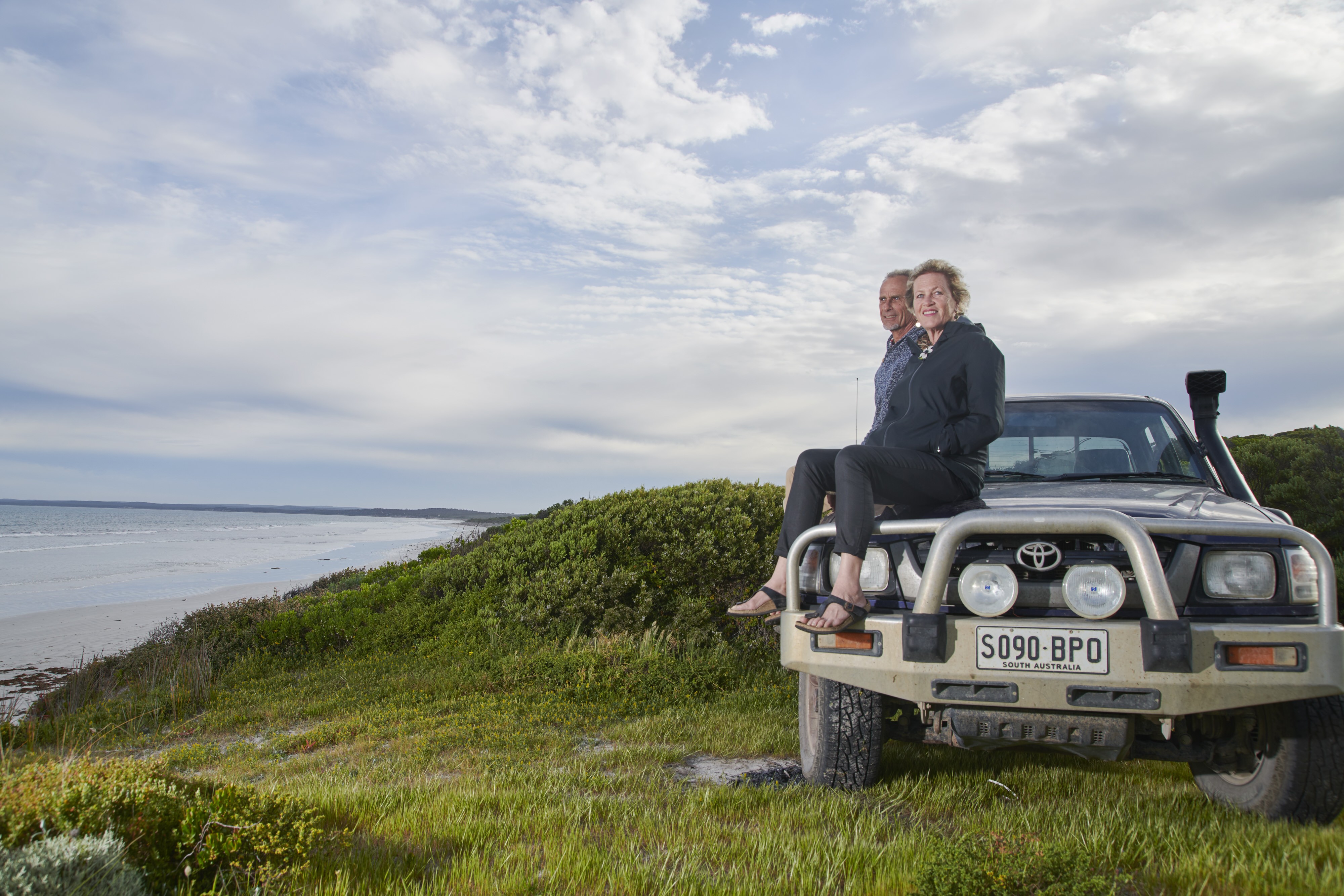 Een stel zit op de motorkap van een auto aan zee in Australië