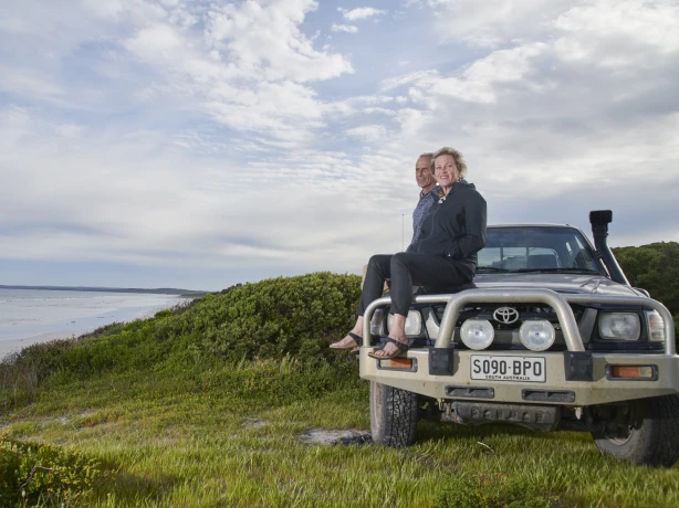 Een stel zit op de motorkap van een auto aan zee in Australië