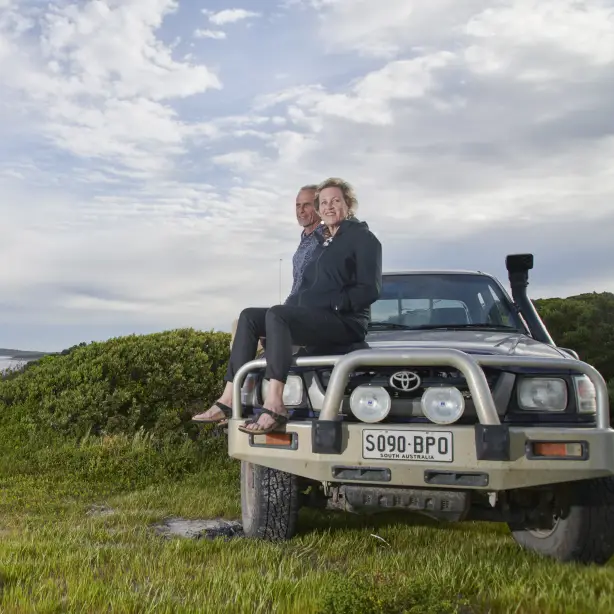 Een stel zit op de motorkap van een auto aan zee in Australië