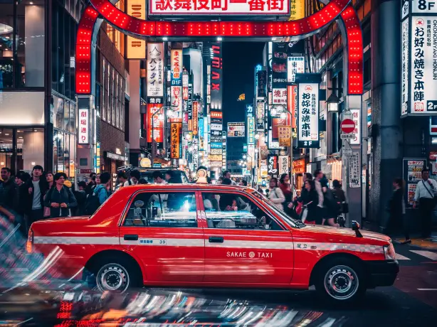 Ein Taxi fährt auf den Straßen von Tokio mit belebten Straßen und Lichtzeichen im Hintergrund