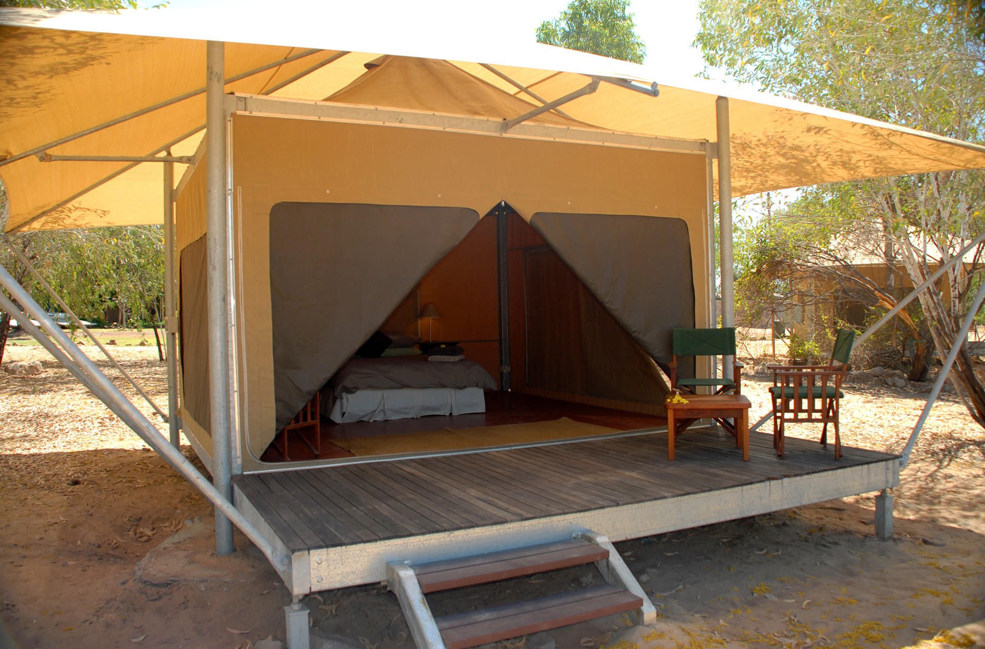 Canvas tent on a raised wooden platform with open front flaps, showing a bed inside and outdoor chairs on the deck.