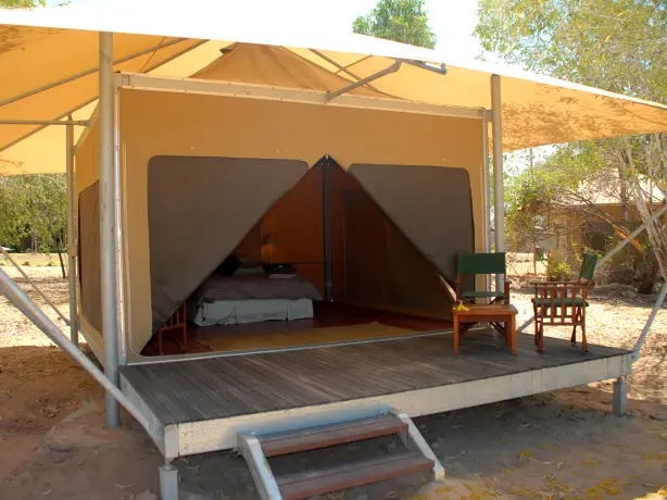 Canvas tent on a raised wooden platform with open front flaps, showing a bed inside and outdoor chairs on the deck.