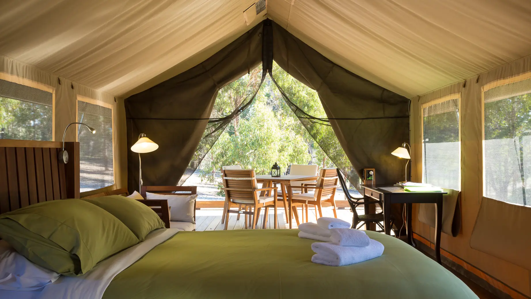Interior of a glamping safari tent with a double bed, sofa, desk, and dining area