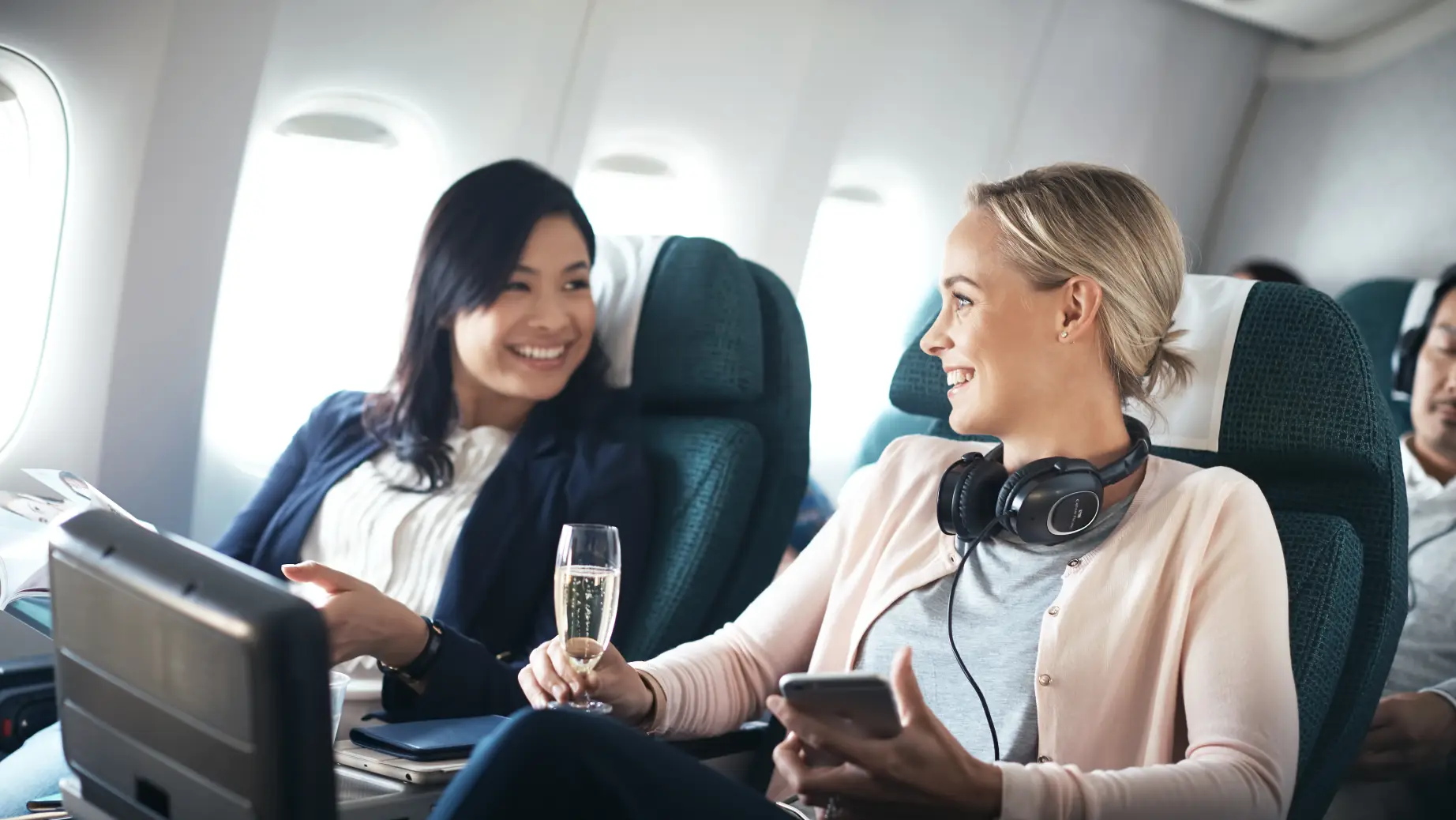 Zwei Frauen sitzen mit Sekt in Flugzeug und lachen