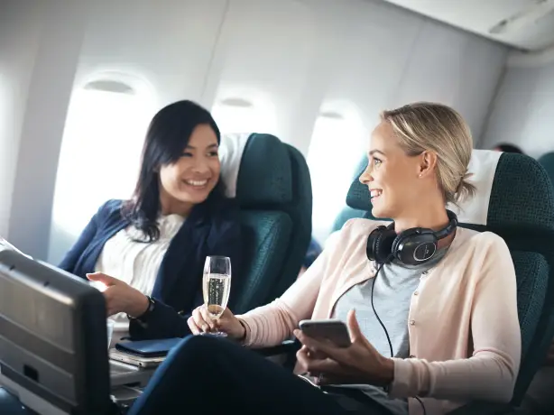Zwei Frauen sitzen mit Sekt in Flugzeug und lachen