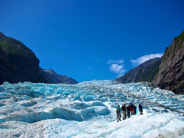 Hikers walking across the blue ice of Fox Glacier in New Zealand