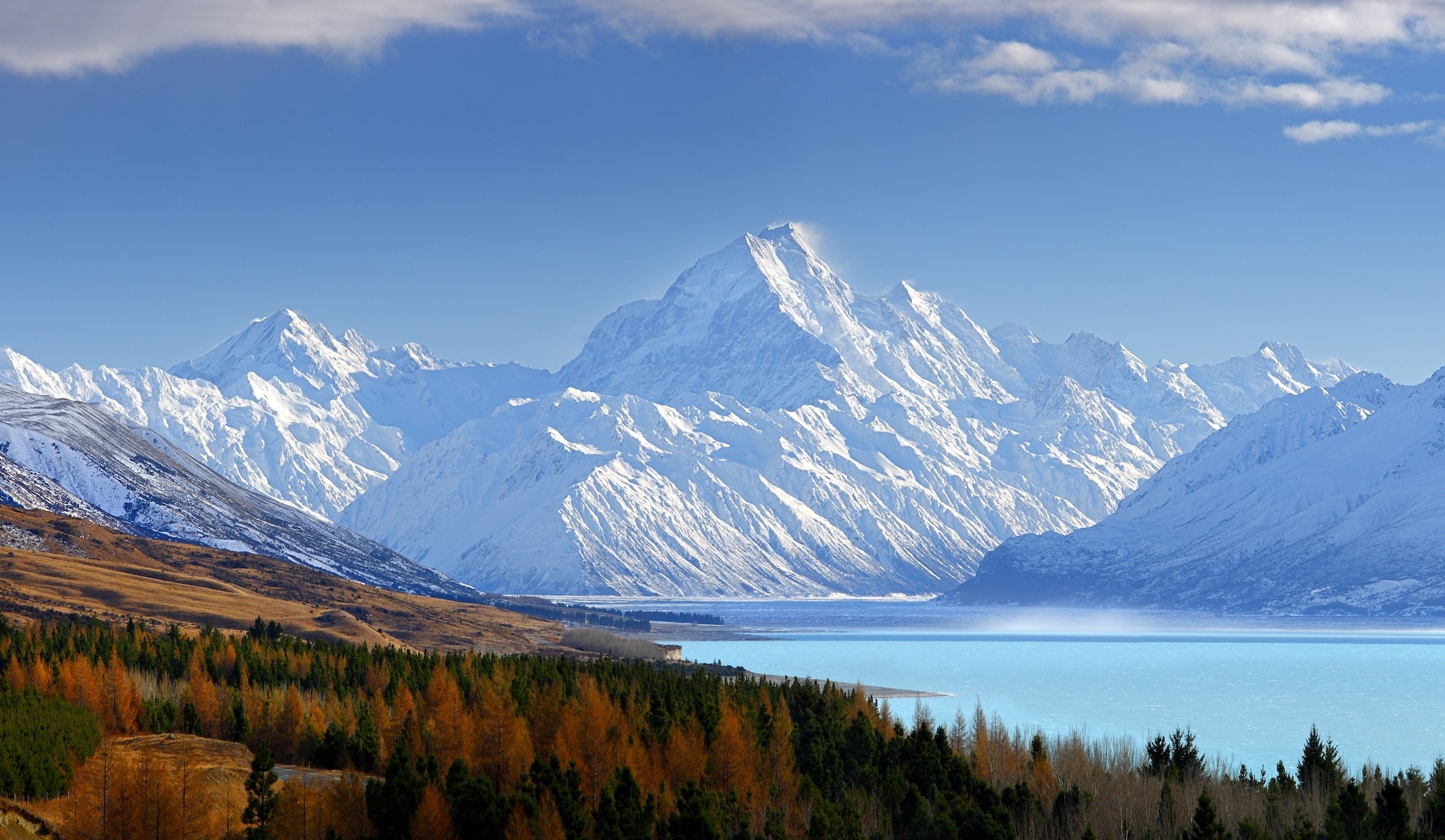 Een blauw meer en een boomgrens met grote besneeuwde bergen op de achtergrond in het Aoraki/Mount Cook National Park in Canterbury