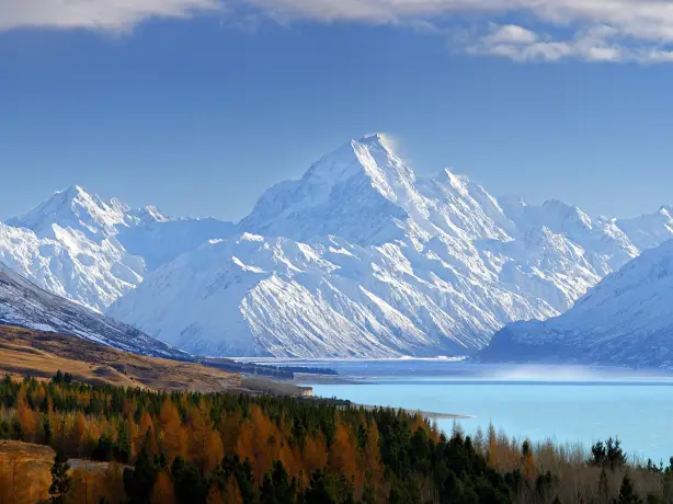 Ein blauer See und eine Baumgrenze mit großen schneebedeckten Bergen im Hintergrund im Aoraki/Mount Cook National Park in Canterbury