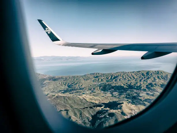 Ausblick aus einem Flugzeugfenster von Air New Zealand auf eine Landschaft mit Bergen und Gewässer