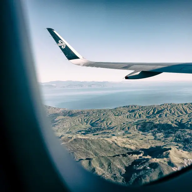 Ausblick aus einem Flugzeugfenster von Air New Zealand auf eine Landschaft mit Bergen und Gewässer