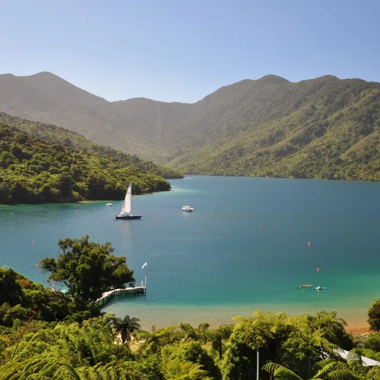 Boats and kayaks on the water surrounded by mountains in the Marlborough sounds in New Zealand