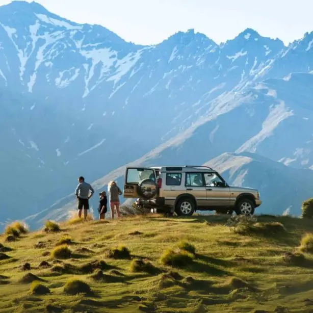 Eine Familie steht neben einem Auto am Rande eines Hügels mit Blick auf die Berge in Neuseeland