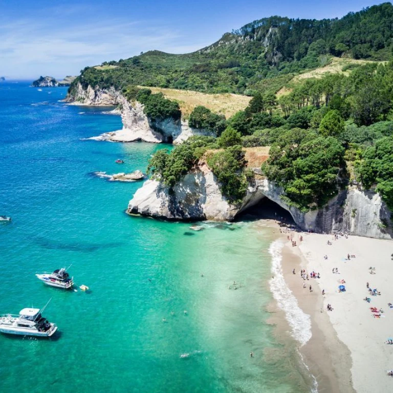 Aerial view of Cathedral Cove, New Zealand with boats moored in sea and people relaxing on the beach