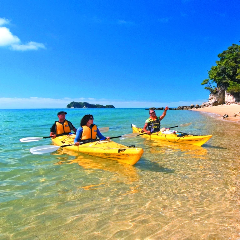 Three people sea kayaking along the coast in Abel Tasman