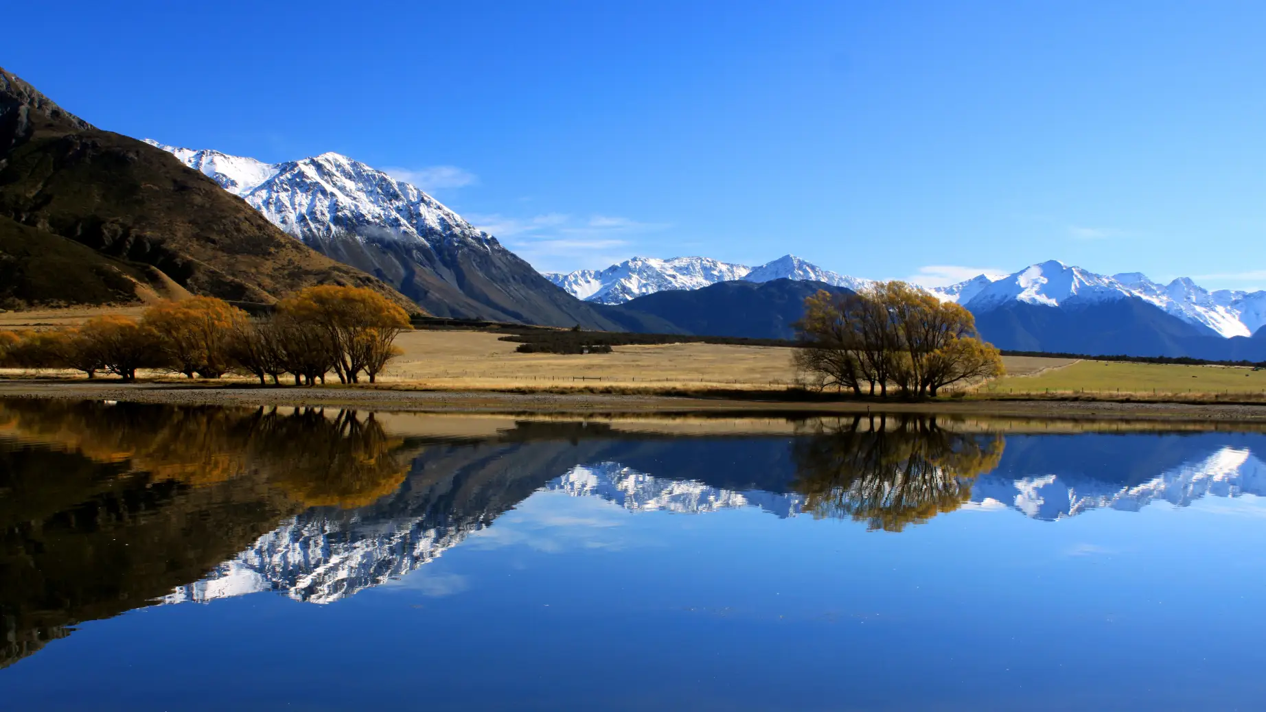 Eine weite Landschaft mit schneebedeckten Bergen, die sich im ruhigen blauen Wasser in Neuseeland spiegeln
