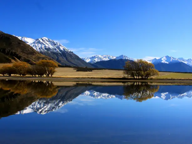 Eine weite Landschaft mit schneebedeckten Bergen, die sich im ruhigen blauen Wasser in Neuseeland spiegeln