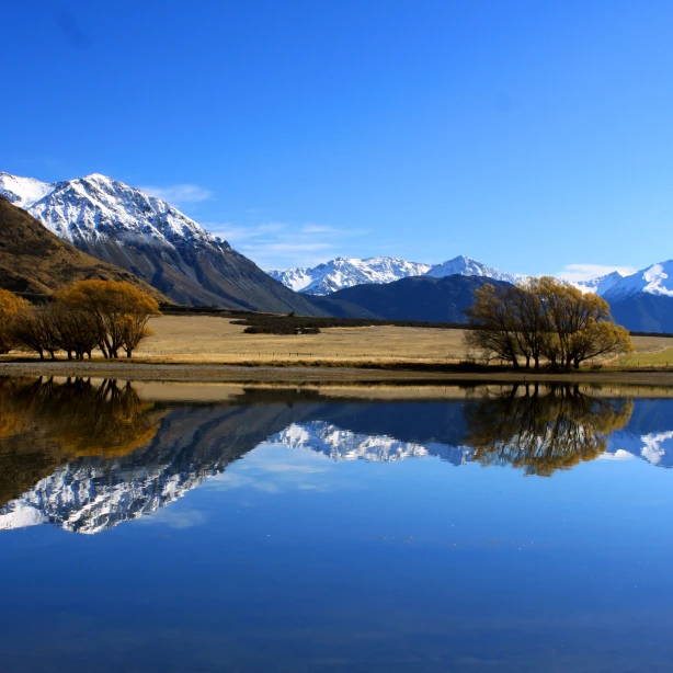 Een weids landschap met besneeuwde bergen die reflecteren in het rimpelloze blauwe water in Nieuw-Zeeland