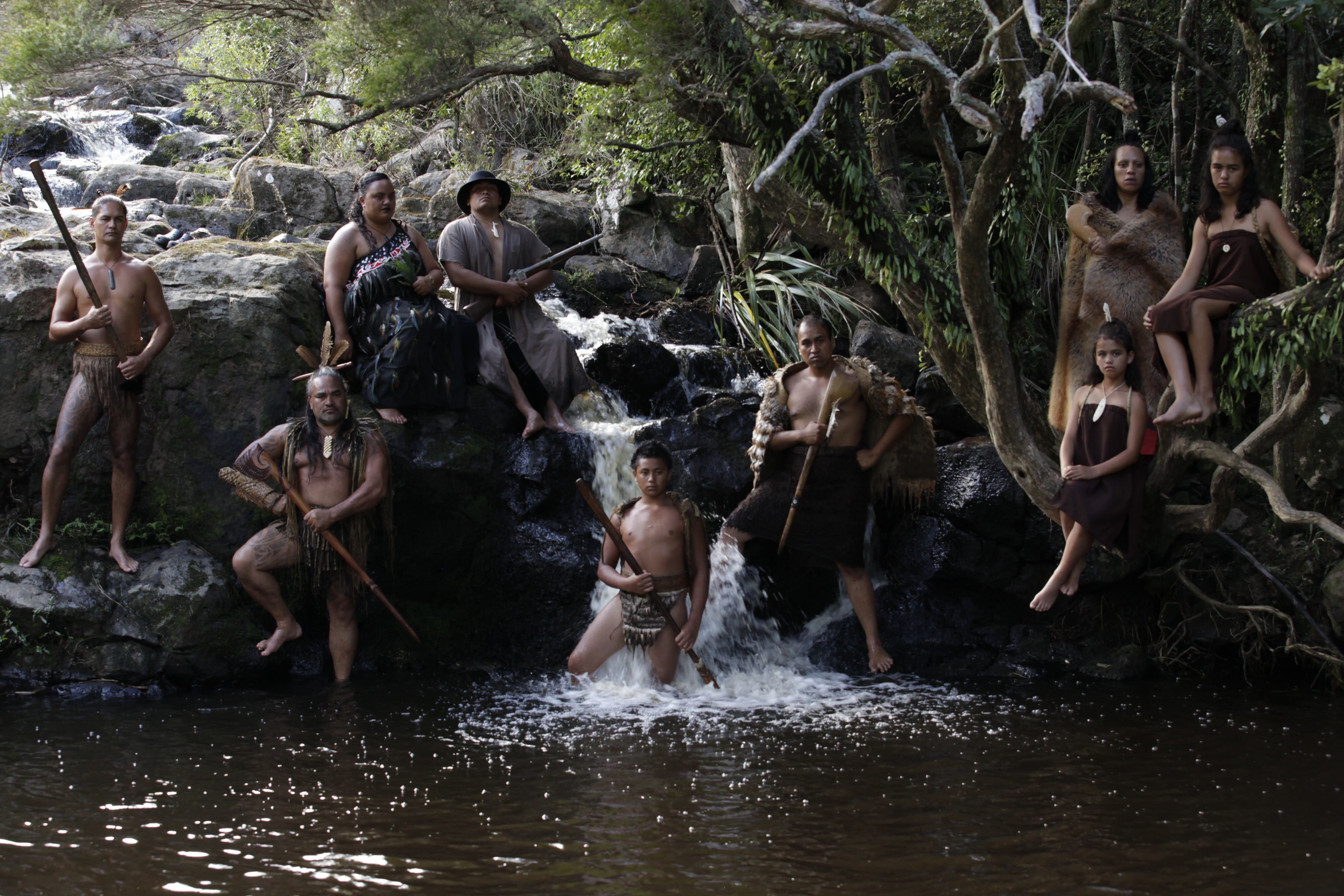 Eine indigene Māori-Familie, die sich an Felsen bei einem kleinen Wasserfall in einem Fluss lehnt