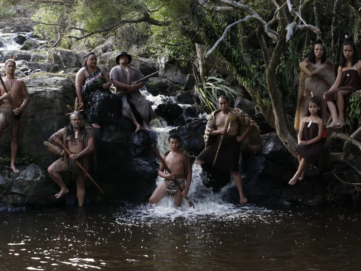 An Indigenous Māori family leaning on rocks near a small waterfall in a river