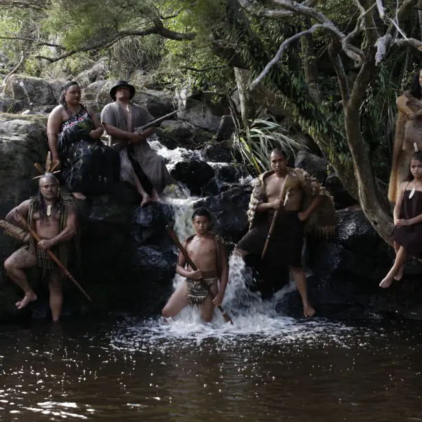 Eine indigene Māori-Familie, die sich an Felsen bei einem kleinen Wasserfall in einem Fluss lehnt
