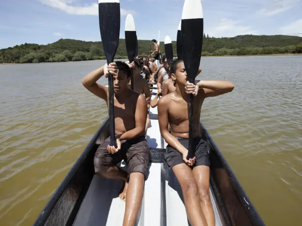 Eine Gruppe Māori-Männer in einem Boot mit schwarzen Paddeln mit weißen Enden