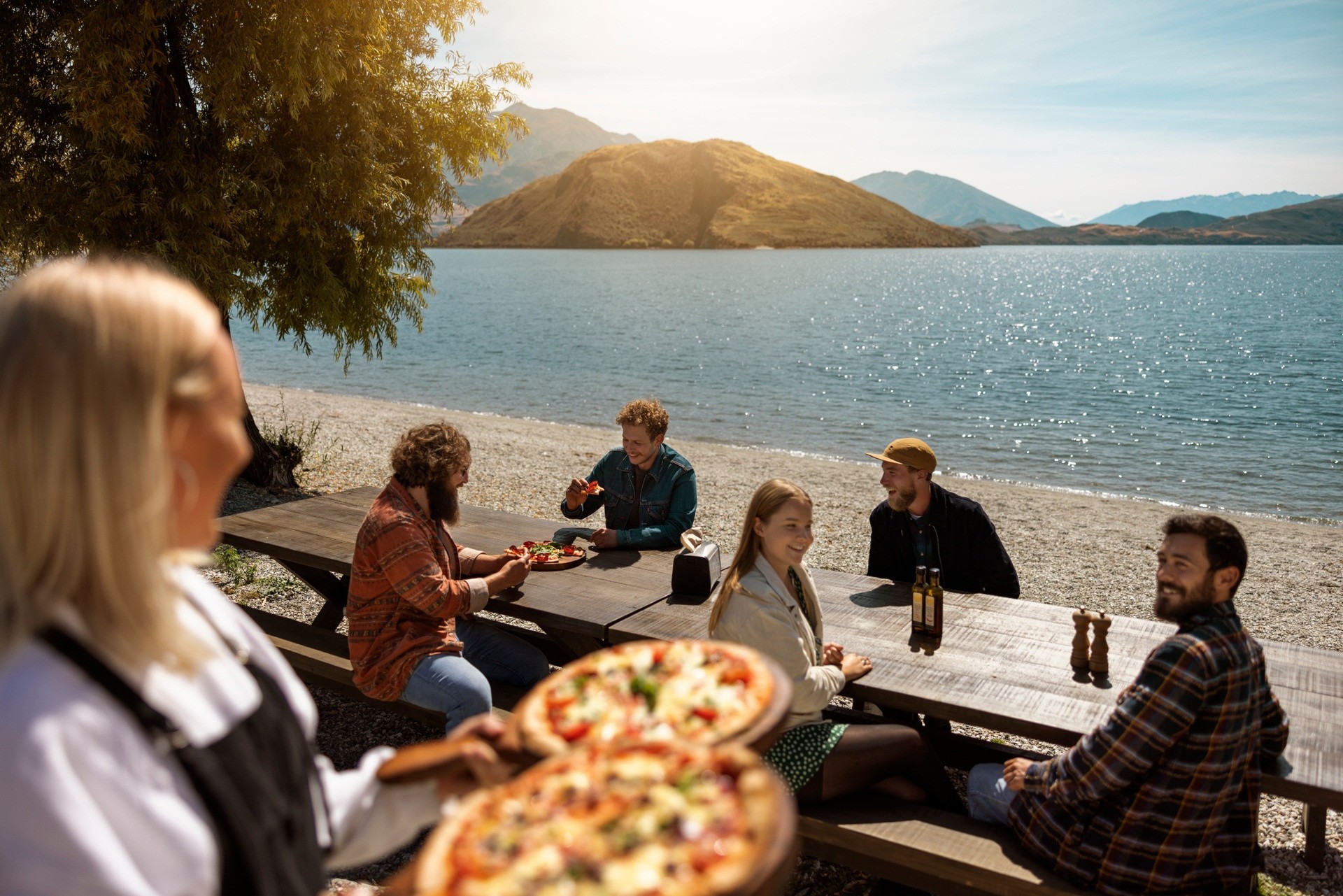 Een groep mensen geniet van drankjes en pizza aan picknicktafels op een terras