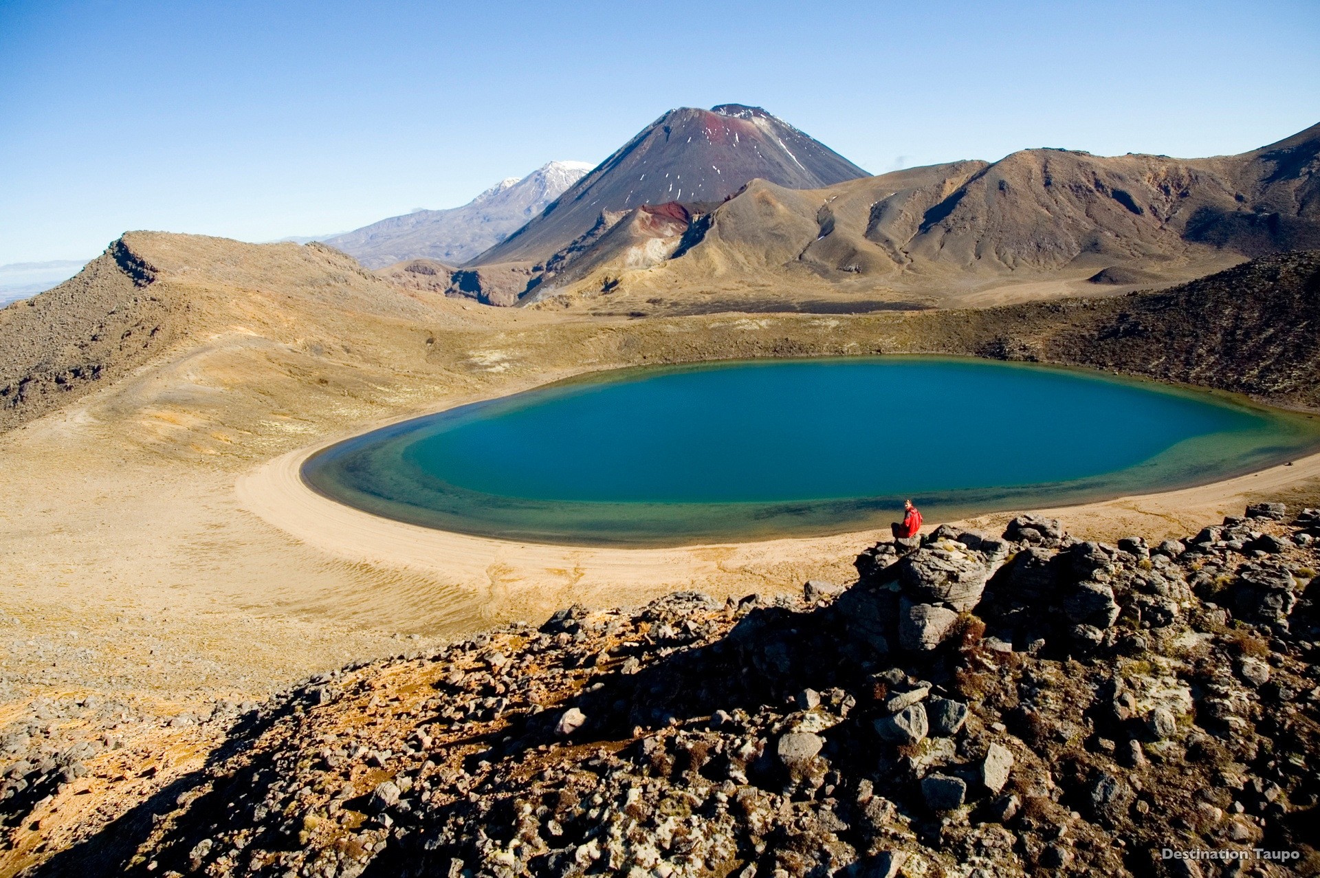 Person, die in einem Felsen sitzt und in die Kamera schaut, vor dem Blue Lake in Tongariro