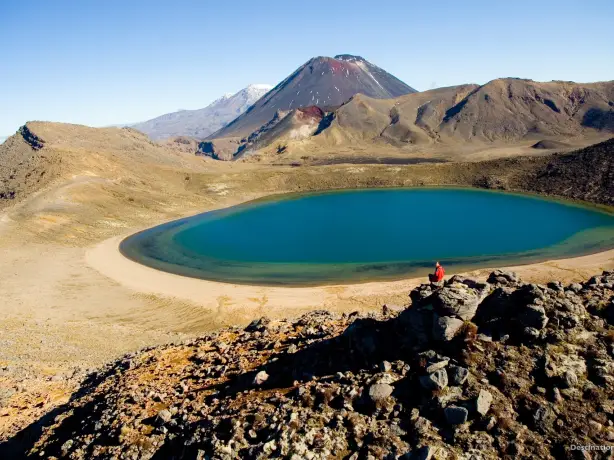 Person, die in einem Felsen sitzt und in die Kamera schaut, vor dem Blue Lake in Tongariro