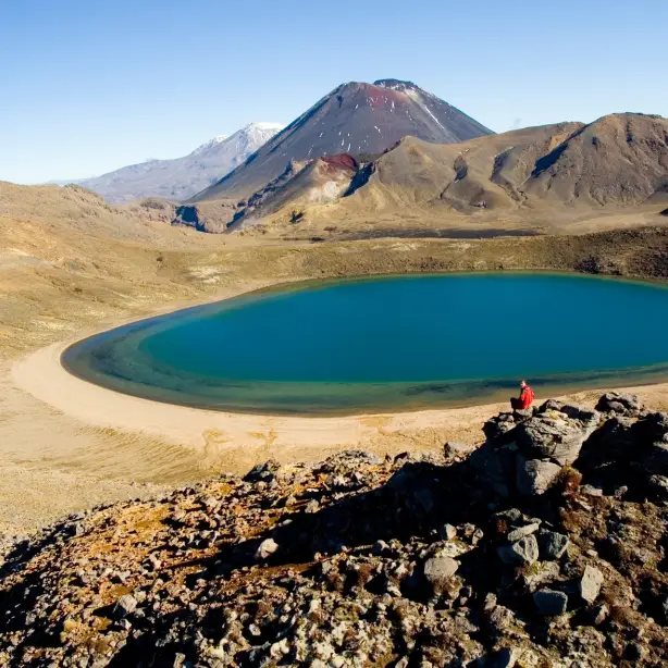 persoon zittend in een rots die terugkijkt naar de camera voor Blue Lake in Tongariro